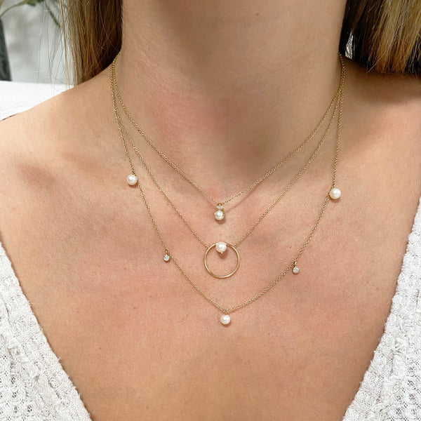woman's neck wearing Zoë Chicco 14kt Gold Floating Pearl Medium Circle Necklace layered with two other pearl and diamond necklaces