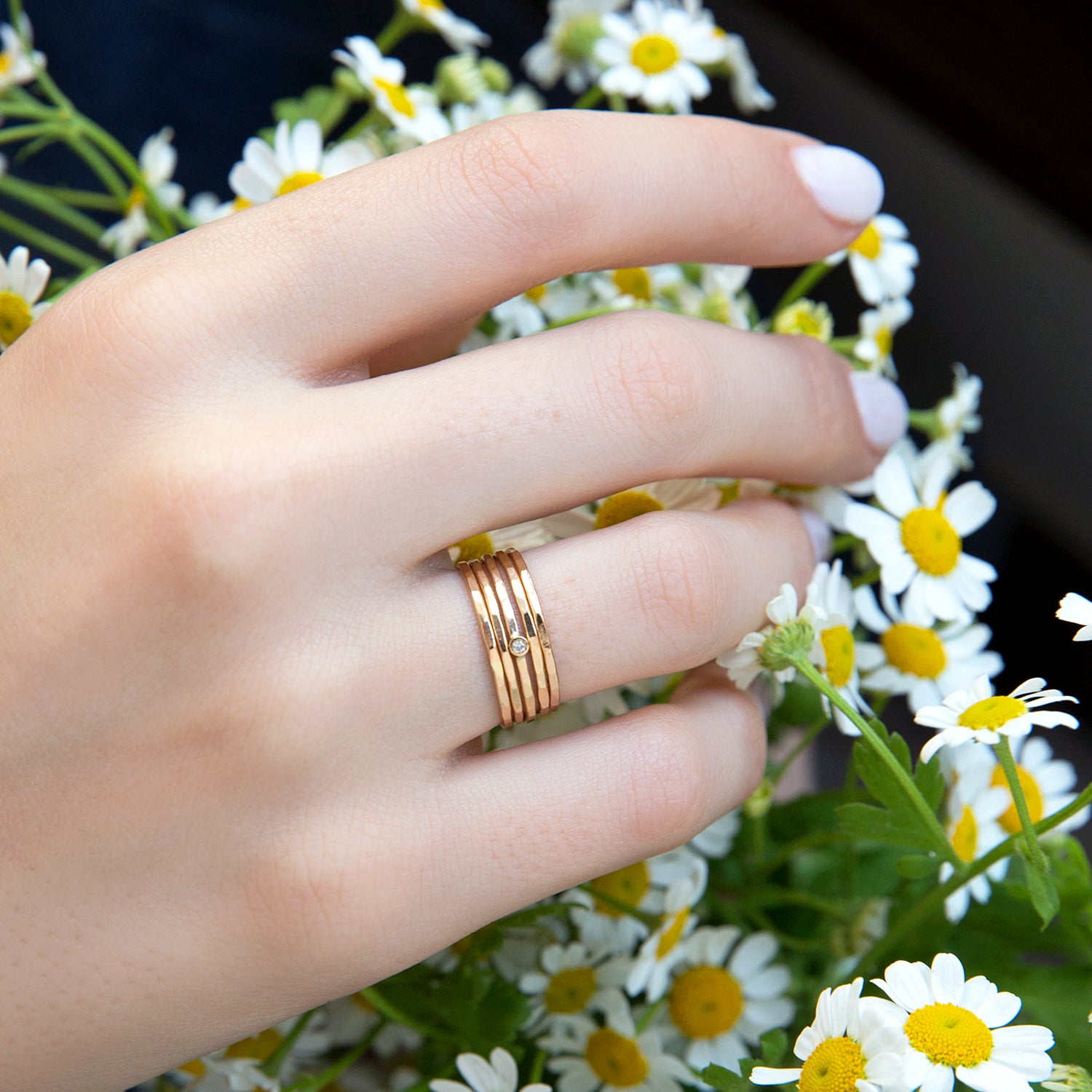 A woman's hand is hovering over flowers with the Set of 5 14k Hammered Gold & Diamond Rings from Zoe Chicco