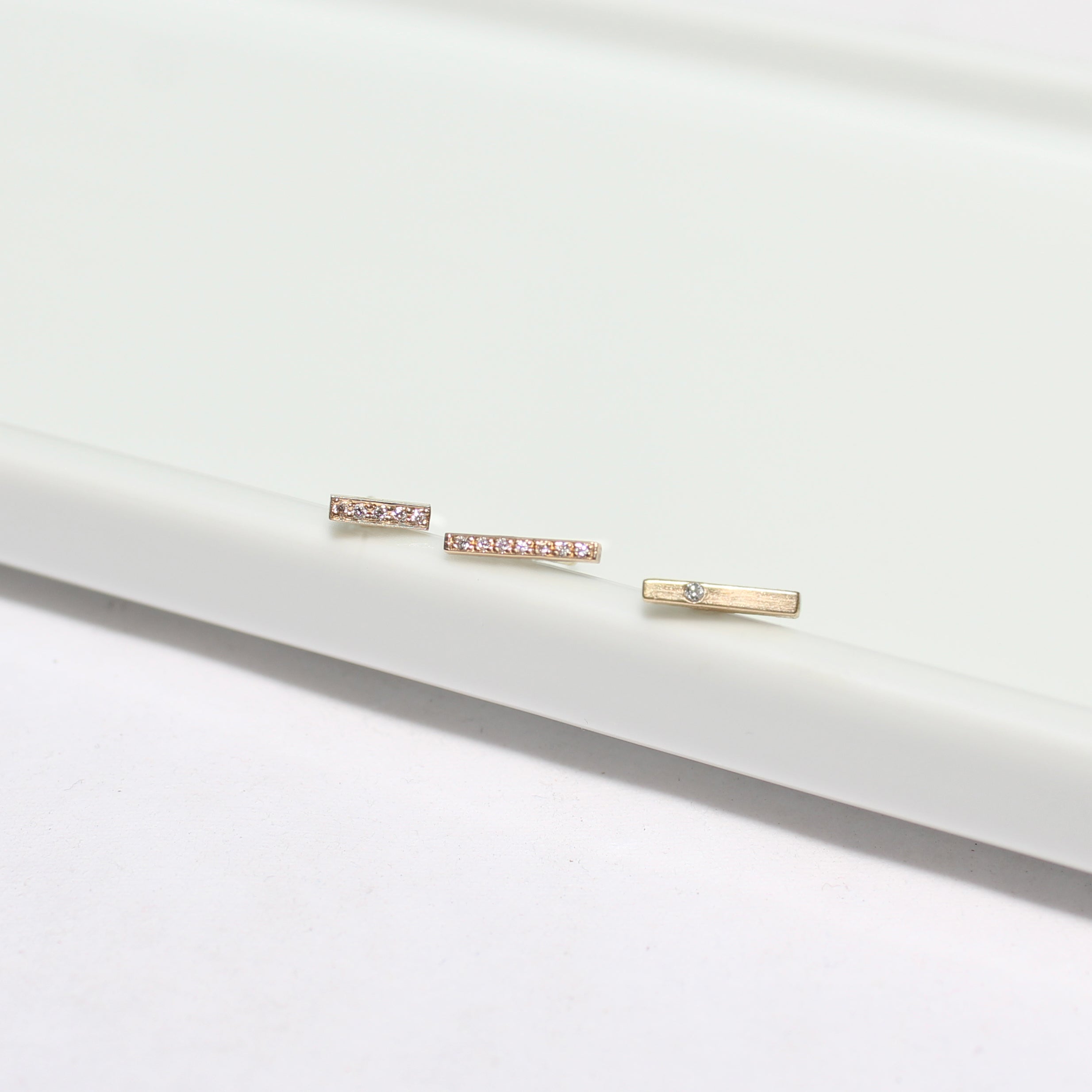 a Zoe Chicco 14k Gold Single Diamond Thin Bar Stud Earring laying with two pave diamond bar stud earrings in a row
