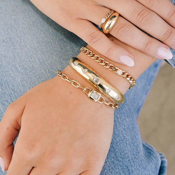 woman resting her hand on her lap wearing a Zoë Chicco 14k Yellow Gold Mixed Cut Diamond Medium Aura Cuff Bracelet stacked with a one of a kind diamond bracelet and a floating diamond large curb chain bracelet