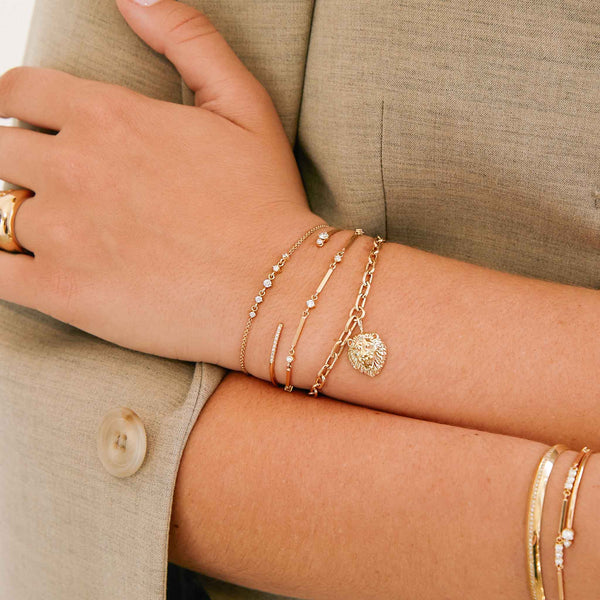 woman in a beige jacket wearing a Zoë Chicco 14k Gold Mixed Prong & Pavé Diamond Cuff Bracelet layered with three other bracelets