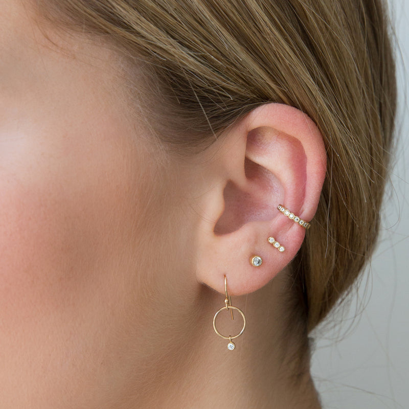 woman's ear wearing Zoë Chicco 14kt Gold Tiny Circle Drop & Dangling Diamond Earrings layered with three other diamond earrings