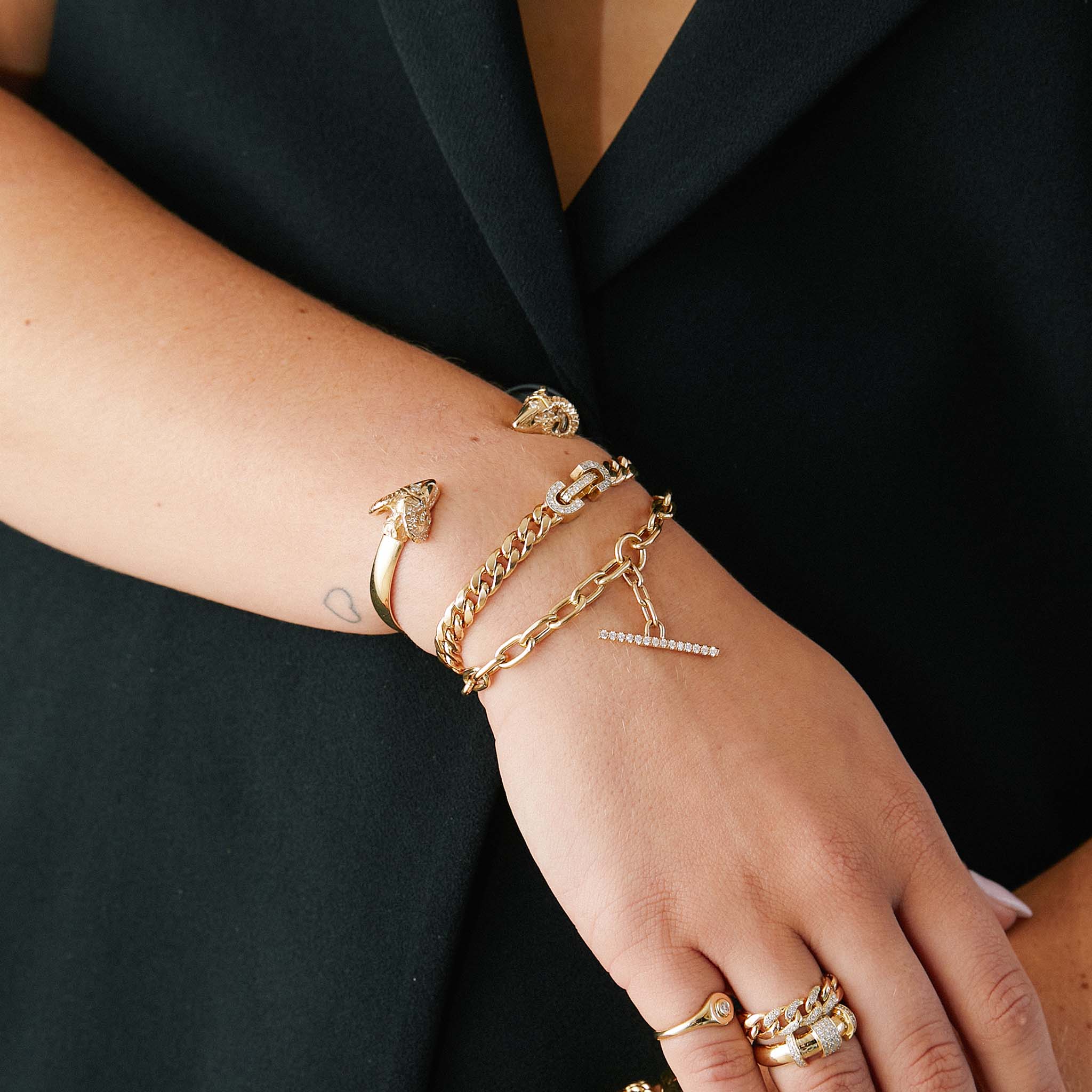 woman in a black vest wearing a Zoë Chicco 14k Gold Vintage Pavé Diamond Horsebit Link Large Curb Chain Bracelet layered with a Rams Head Cuff and a Pave Diamond Toggle Bracelet