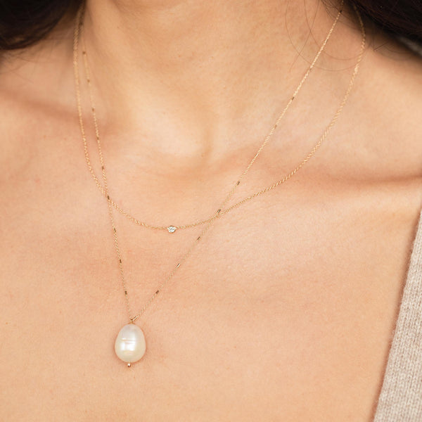 close up of woman wearing a Zoë Chicco 14k Gold Floating Diamond & Large Baroque Pearl Layered Necklace