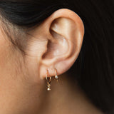woman's ear wearing a Zoë Chicco 14k Gold Dangling Diamond Bezel Thin Huggie Hoop Earring