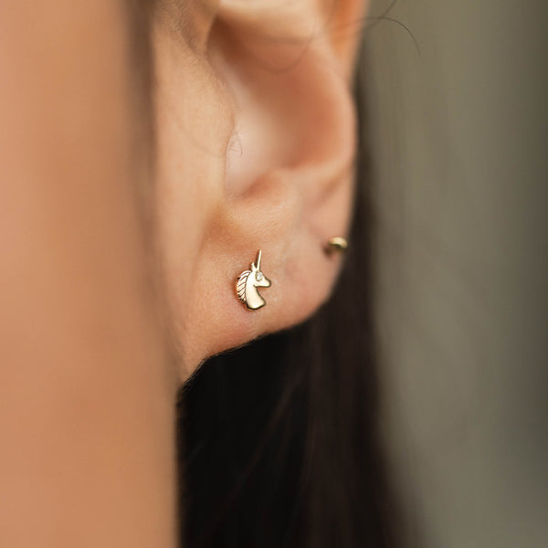 close up of a woman's ear wearing a Zoë Chicco 14k Gold Itty Bitty Unicorn with Diamond Eye Stud Earring