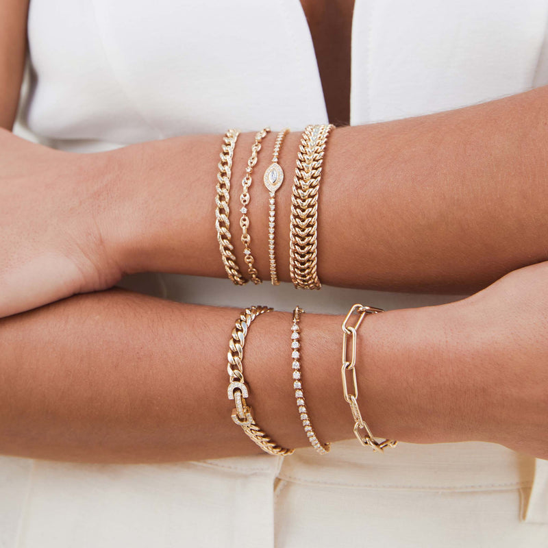 woman with her arms crossed in front of her wearing a Zoë Chicco 14k Gold Marquise Diamond Halo Tennis Bracelet layered with three other heavy chain bracelets