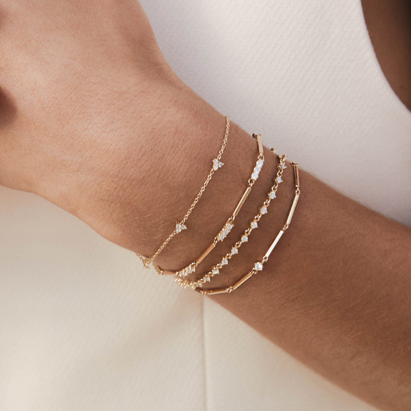 close up of a woman's wrist wearing a Zoë Chicco 14k Gold Single Diamond Gold Linked Bar Bracelet layered with three other gold and diamond bracelets