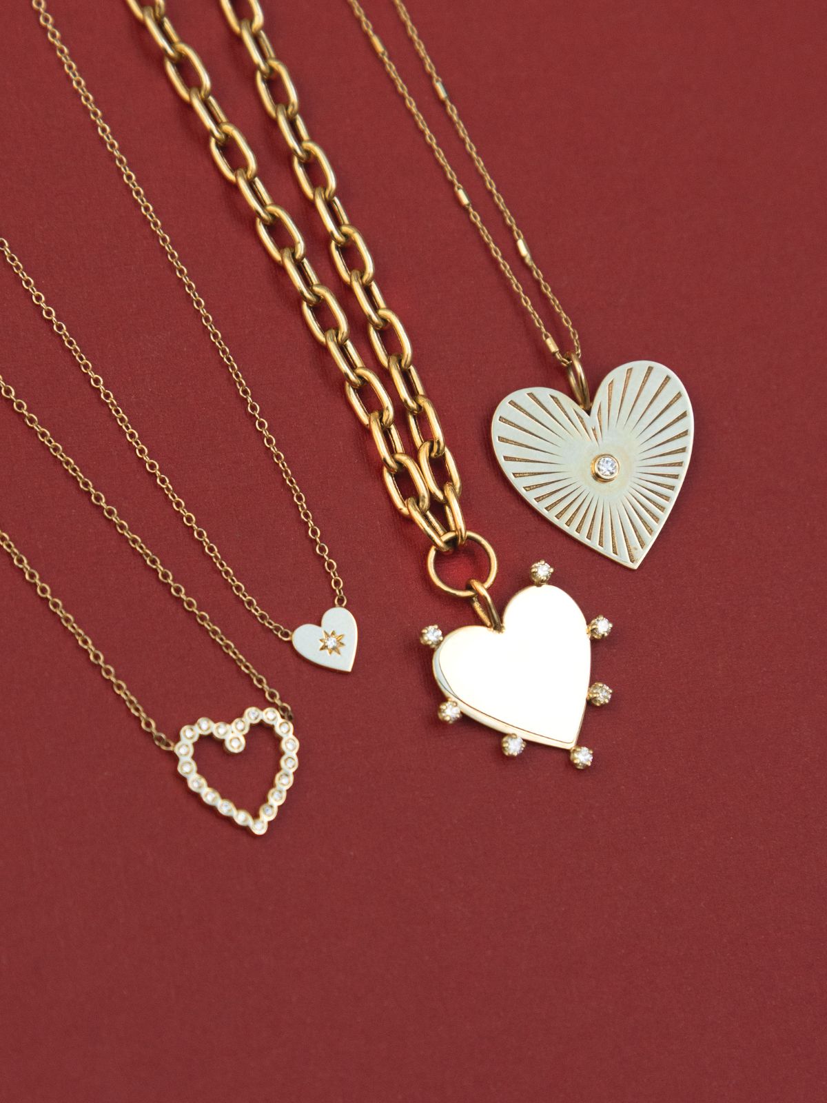 Three Zoe Chicco 14k gold and diamond necklaces for the Tokens of Love Gift Guide laying against a pink background