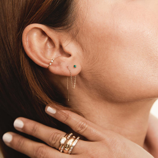 Close-up of an ear with Zoe Chicco 14k gold chain and hoop earrings and a hand wearing gold rings.