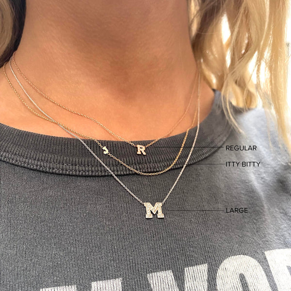 comparison image of a woman wearing an itty bitty initial necklace with a regular and large pavé diamond initial letter necklace layered together