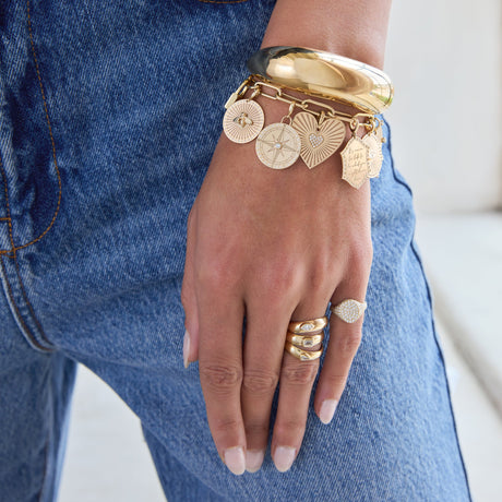 Zoe Chicco 14K Gold charm bracelet and rings on a hand with blue jeans