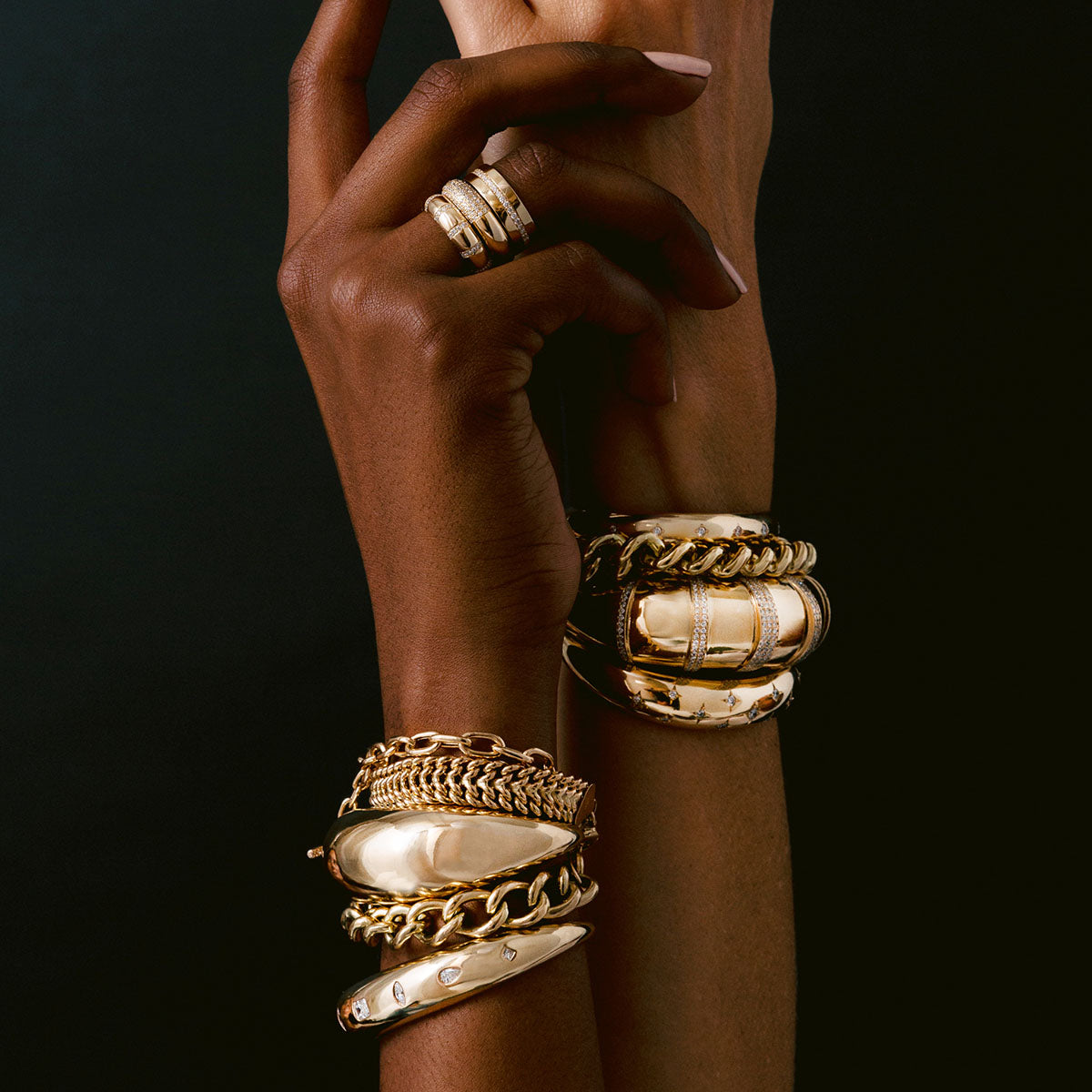 Hand wearing multiple Zoe Chicco 14k gold bracelets and rings against a black background