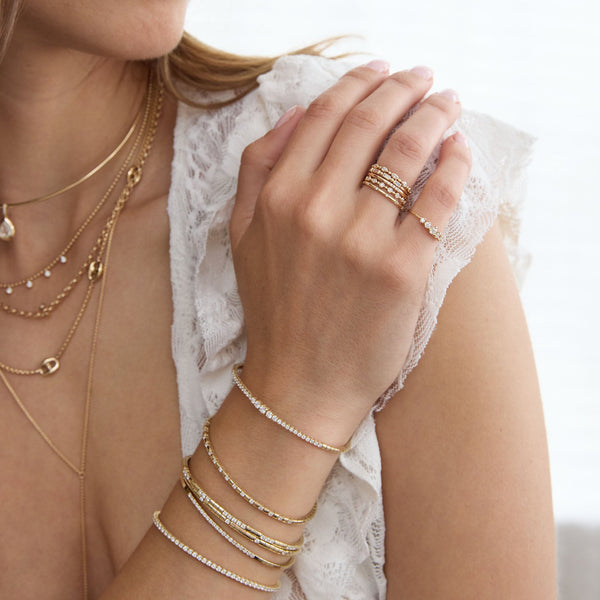 Close-up of a person wearing multiple Zoe Chicco 14k gold bracelets and rings on a white background