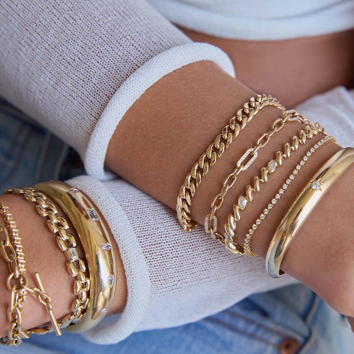 Close up of wrists wearing Zoe Chicco 14k gold bracelets on a light background