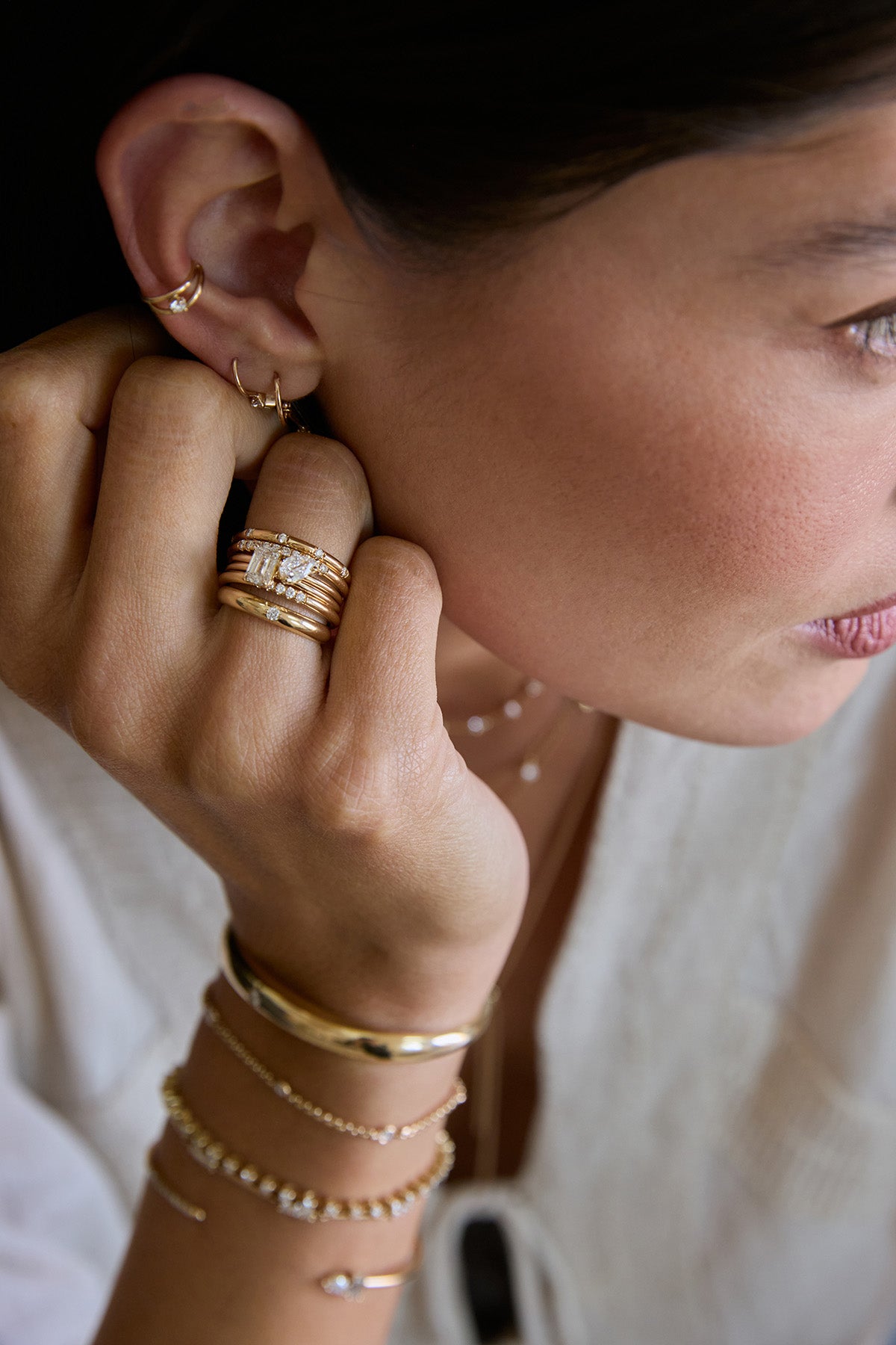 Close-up of a woman wearing a stack of Zoe Chicco 14k gold rings with emerald cut and pear cut diamonds with layers of gold bracelets