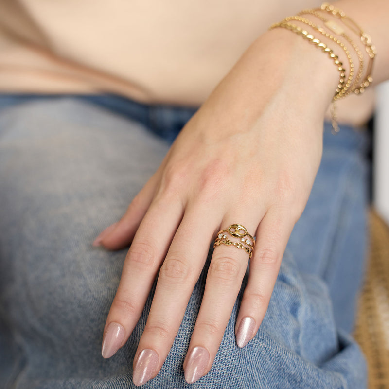 Close-up of a hand with multiple Zoe Chicco 14k gold and diamond rings and bracelets on a blurred denim background