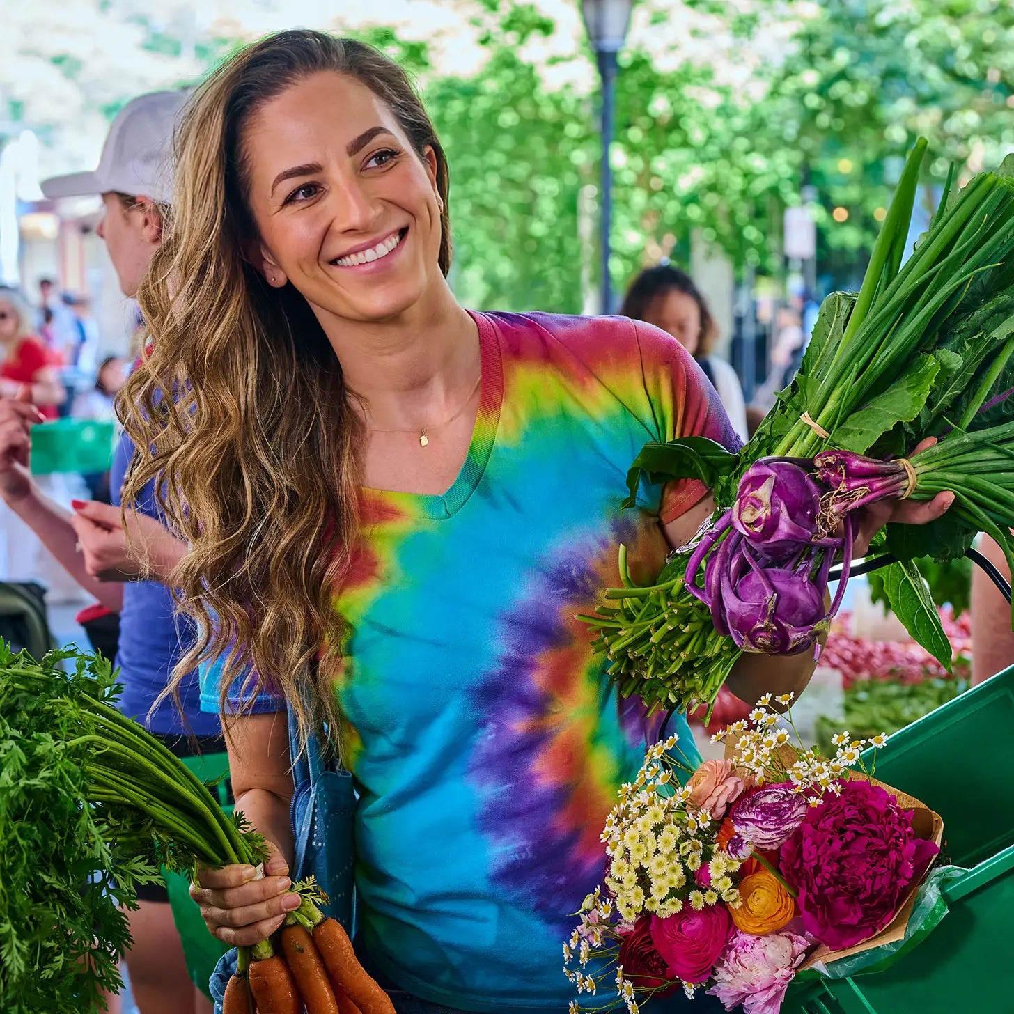 Melissa Benishay wearing a tie-dye shirt and a 14K gold Zoe Chicco midi bitty lemon charm necklace holding produce at an outdoor market