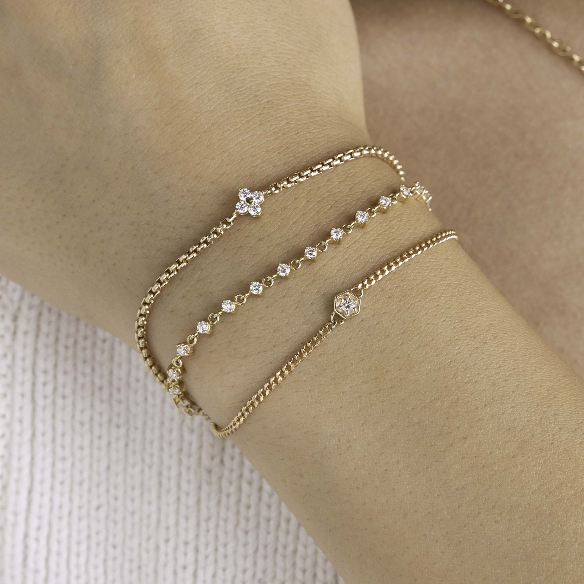 A woman is wearing a Zoe Chicco bracelet stack  including 14k Prong Diamond Quad Box Chain Bracelet, 14k Linked Prong Diamond Tennis Bracelet, and 14k Gold Diamond Hexagon Curb Chain Bracelet