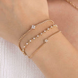 A woman is wearing a Zoe Chicco bracelet stack  including 14k Prong Diamond Quad Box Chain Bracelet, 14k Linked Prong Diamond Tennis Bracelet, and 14k Gold Diamond Hexagon Curb Chain Bracelet