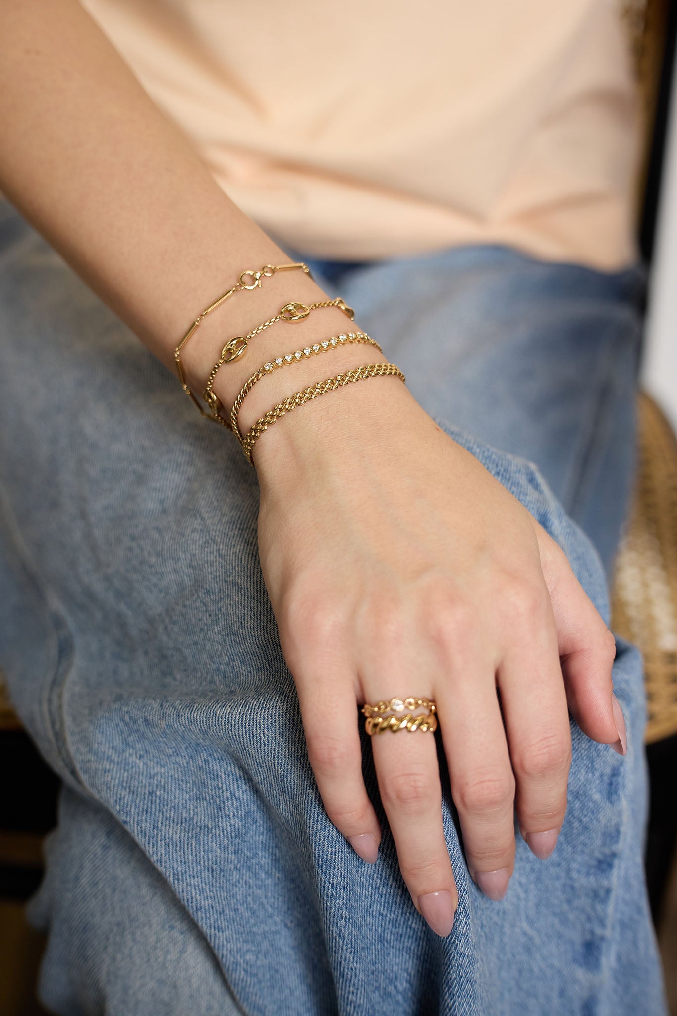 Close up of hand wearing Zoe Chicco 14k gold bracelets and rings on denim background