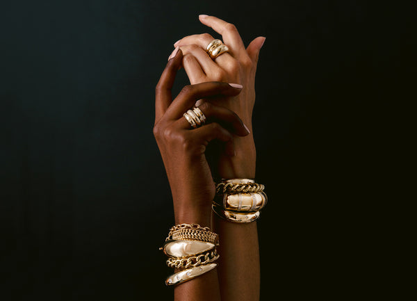 Two hands with Zoe Chicco 14k gold and diamond rings and bracelets against a black background