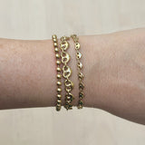 Gold bracelets on a wrist against a neutral background