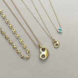 Three gold heart mariner necklaces and a turquoise cluster necklace with emerald and diamond gemstones on a gray background