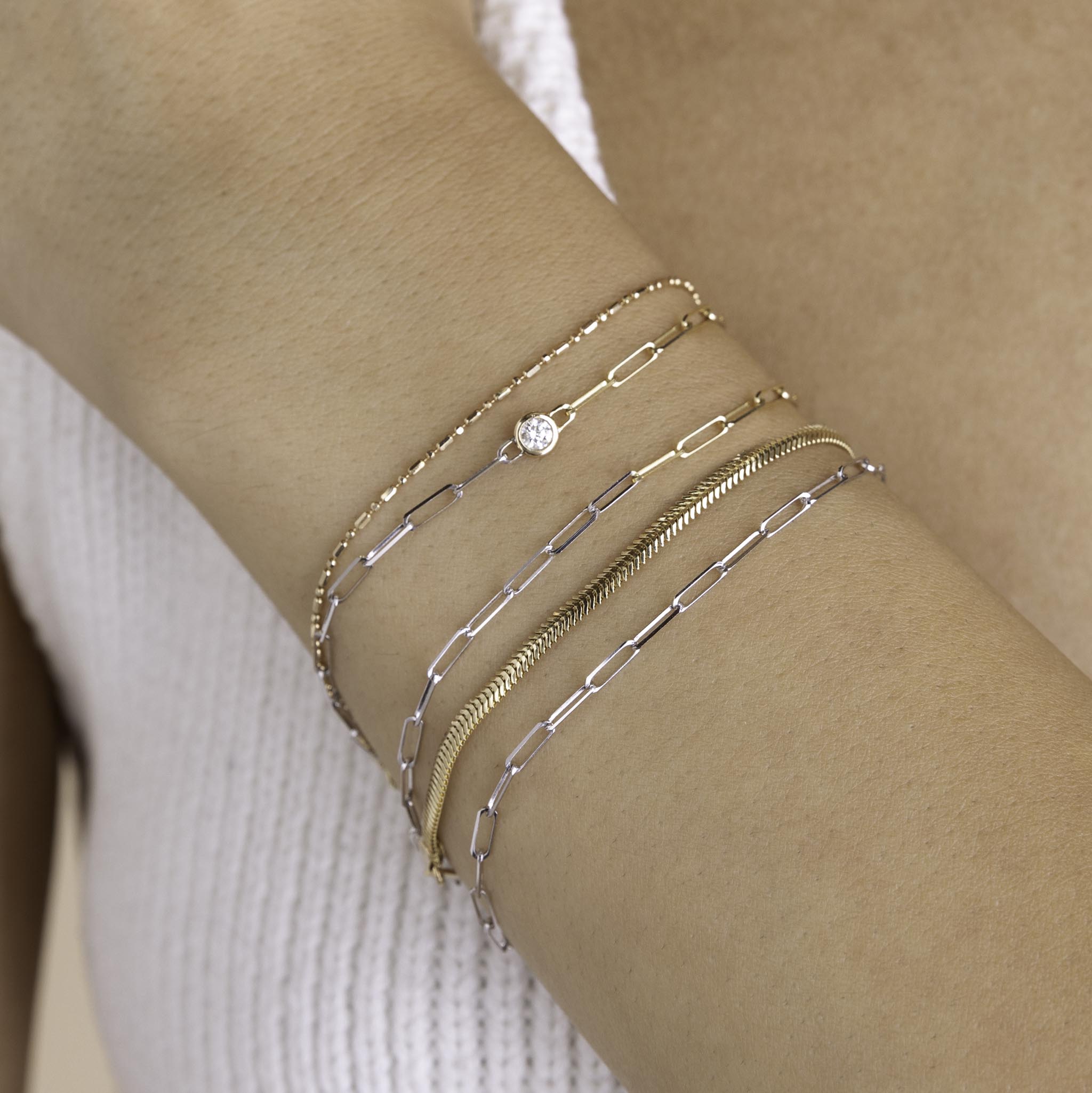 A woman is wearing Zoe Chicco wrist stack including 14k Two Tone Gold Small Paperclip Chain Bracelet, 14k Floating Diamond Two Tone Gold Small Paperclip Chain Bracelet, and small snake chain bracelet.