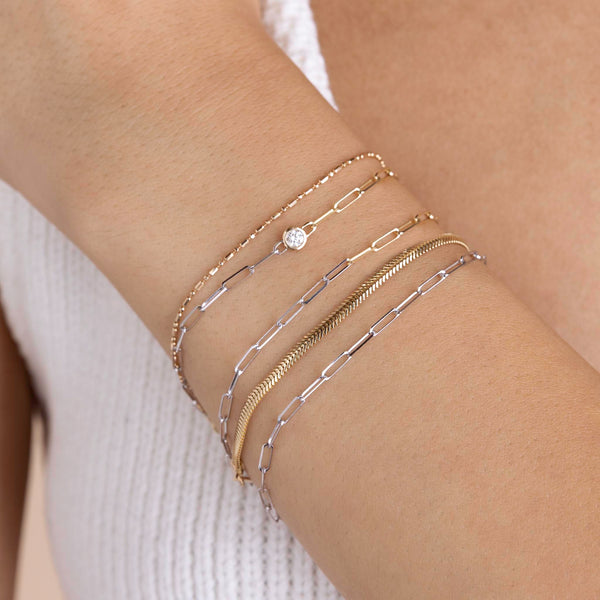 A woman is wearing Zoe Chicco wrist stack including 14k Two Tone Gold Small Paperclip Chain Bracelet, 14k Floating Diamond Two Tone Gold Small Paperclip Chain Bracelet, and small snake chain bracelet.