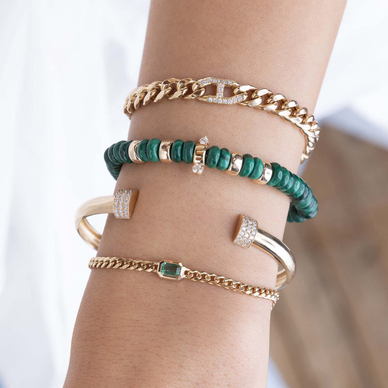 close up of a woman's wrist wearing a Zoë Chicco 14k Gold & Malachite Rondelle Bead Bracelet with 2 Prong Diamonds stacked with a 14k Small Curb Chain Emerald Cut Emerald Bezel Bracelet, 14k Pavé Diamond Door Knocker Cuff, and a 14k Pavé Diamond Mariner Link Large Curb Chain Bracelet