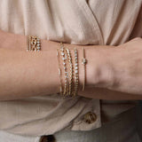 woman's wrist wearing a Zoë Chicco 14k Gold Emerald Cut Diamond Medium Box Chain Bracelet layered with a 14k Curb Chain & Emerald Cut Diamond Half Tennis Bracelet, Baguette Diamond San Marco Chain Bracelet, 14k 3 Diamond Bezel Bar Open Cuff, 14k Linked Graduated Prong Diamond Tennis Bracelet, and a 14k Prong Diamond Bar Station Small Paperclip Chain Bracelet