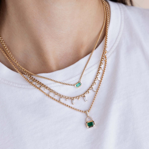 woman in a white tshirt wearing a Zoë Chicco 14k Gold Emerald Cut Emerald & Pavé Diamond Bail Box Chain Necklace stacked with an Emerald cut Emerald Bezel Curb Chain Necklace and a 14k Alternating Baguette & Prong Diamond Box Chain Necklace