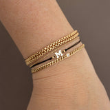 A woman wears a stack of bracelets including 14k Initial Letter Cord Bracelet