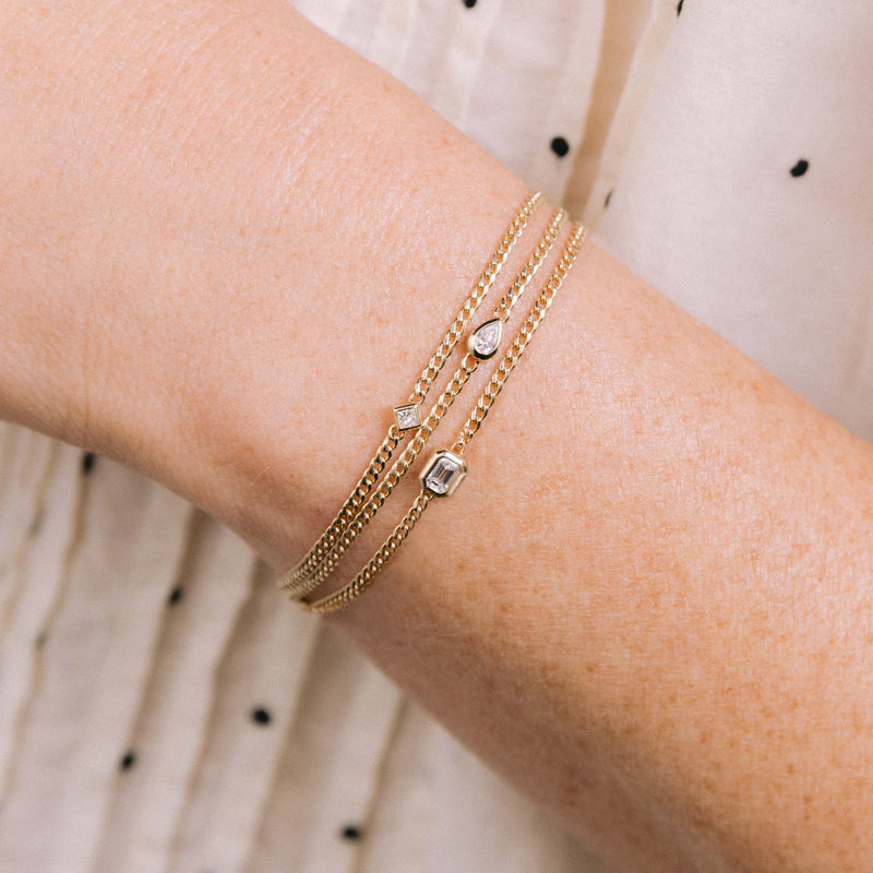 A woman wears a stack of Zoe Chicco bracelets including princess diamond, pear diamond and emerald-cut diamond on XS curb chain.