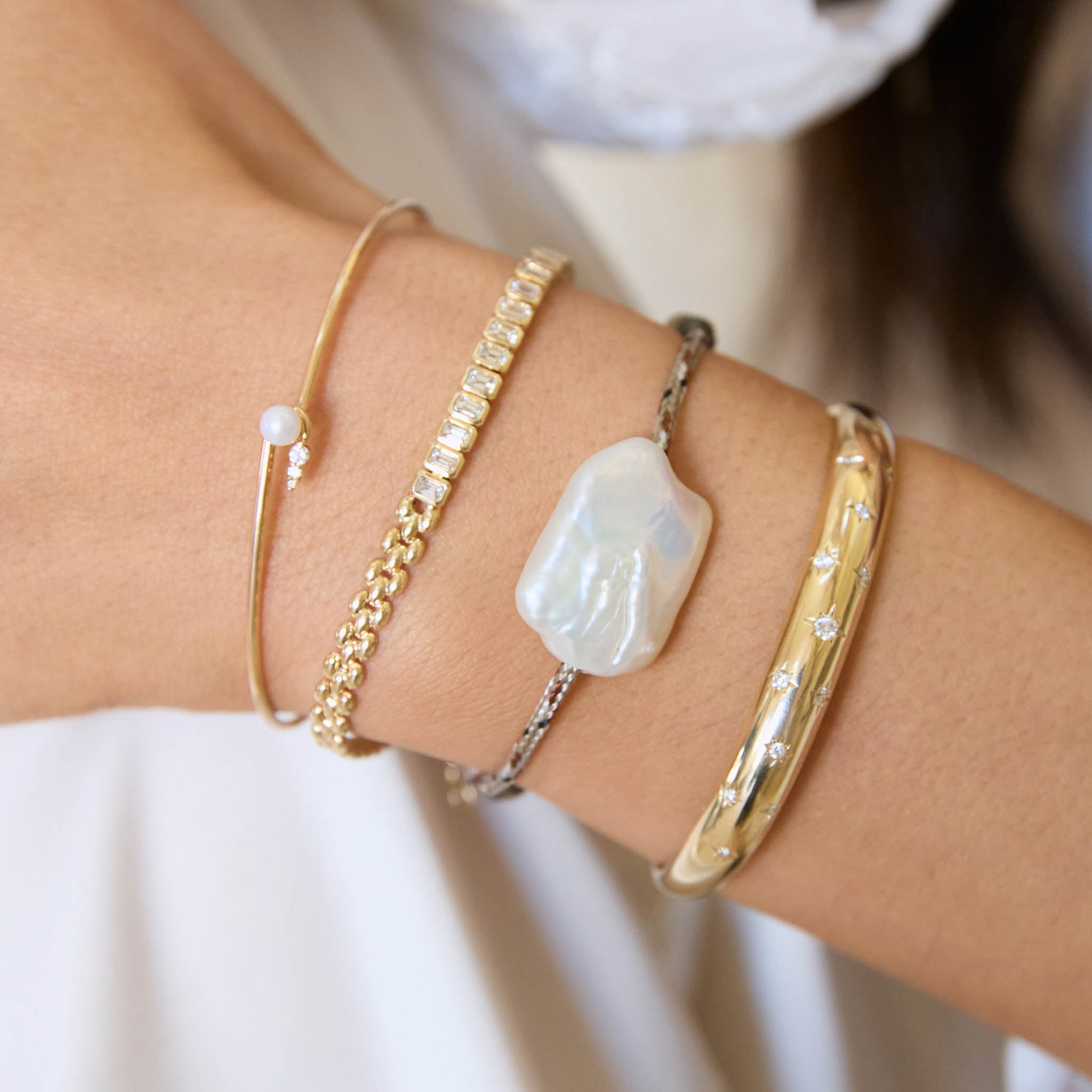 Close-up of a wrist wearing multiple gold bracelets with different designs.
