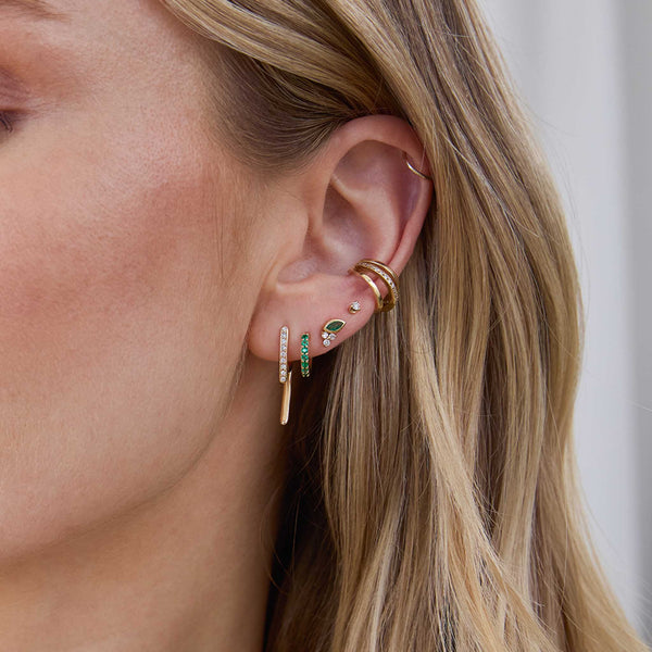 Close up of a woman's ear wearing a Zoë Chicco 14k Gold & Pavé Diamond Talon Earring layered with a 14k Prong Emerald Small Hinge Huggie Hoop and a 14k Marquise Emerald & Diamond Trio Stud in her secondary piercings