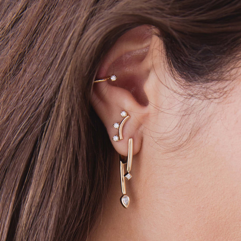 close up of a woman's ear wearing a Zoë Chicco 14k Gold 3 Prong Diamond Curved Bar Stud Earring in her second piercing layered with a 14k Princess & Pear Diamond Talon Earring