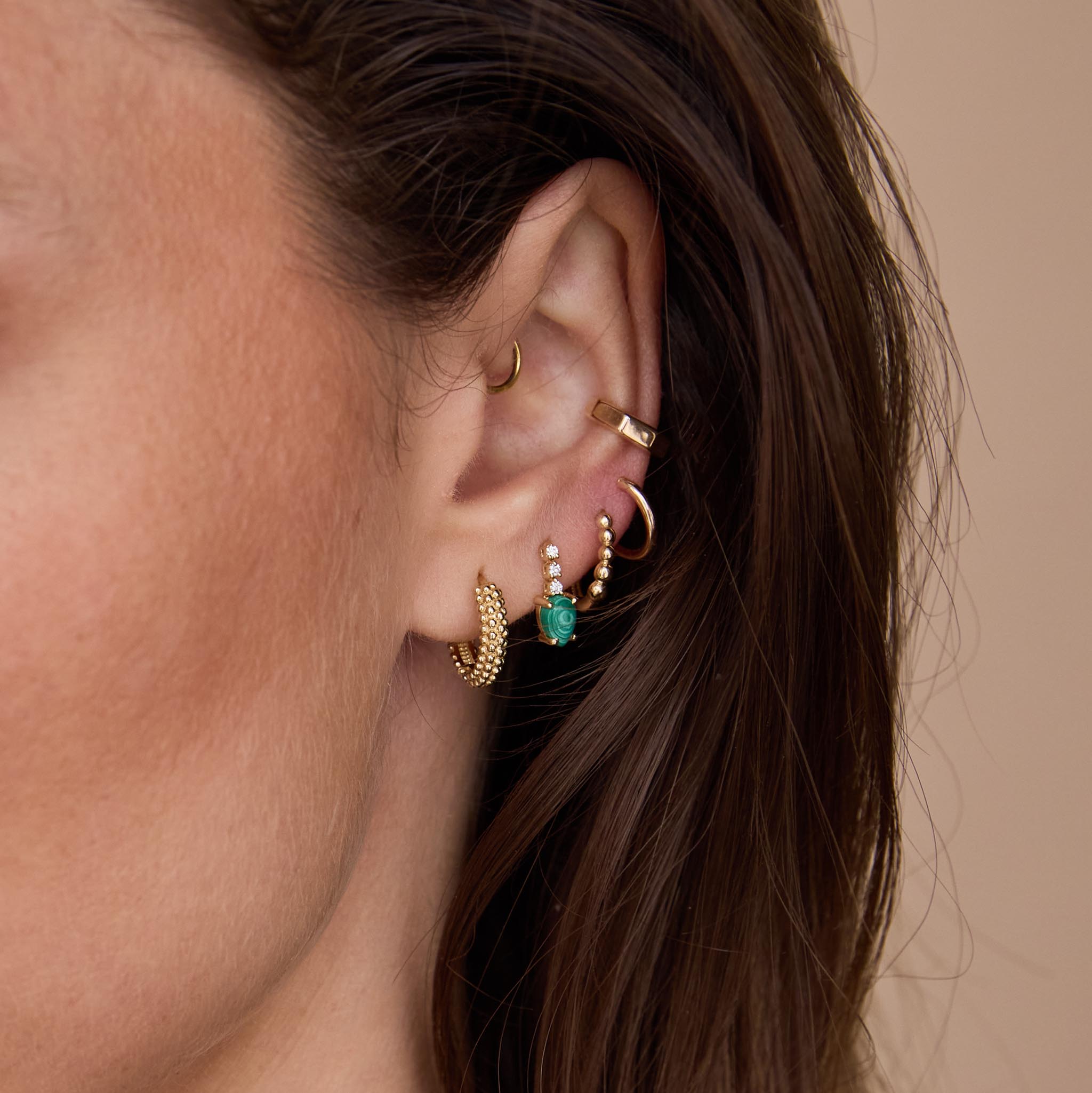 Close-up of an ear with multiple gold and gemstone earrings on a neutral background featuring 14k Pear Malachite Short Diamond Tennis Drop Earrings