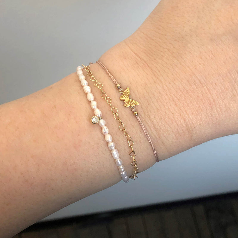 close up of a Zoë Chicco 14k Gold Diamond Charm Rice Pearl Bracelet stacked with a Midi Bitty Butterfly Silk Cord Bracelet and an Open Heart Link Bracelet