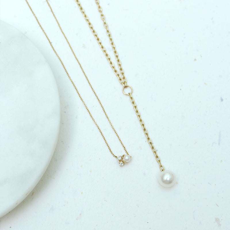 a Zoë Chicco 14k Gold Small Oval Link Chain Lariat with Pearl Drop laying flat against a white stone background