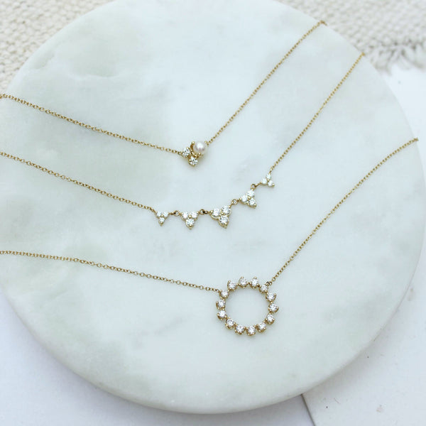 a Zoë Chicco 14k Gold Mixed Prong Diamond & Pearl Cluster Necklace sitting in a marble tray with two other diamond necklaces