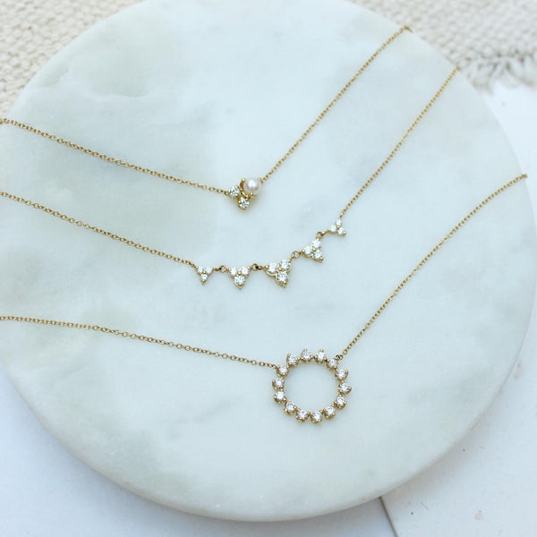 a Zoë Chicco 14k Gold 5 Linked Graduated Diamond Trio Necklace, 14k Prong Diamond Circle Necklace, and Mixed Prong and Diamond Cluster Necklace sitting flat in a marble tray
