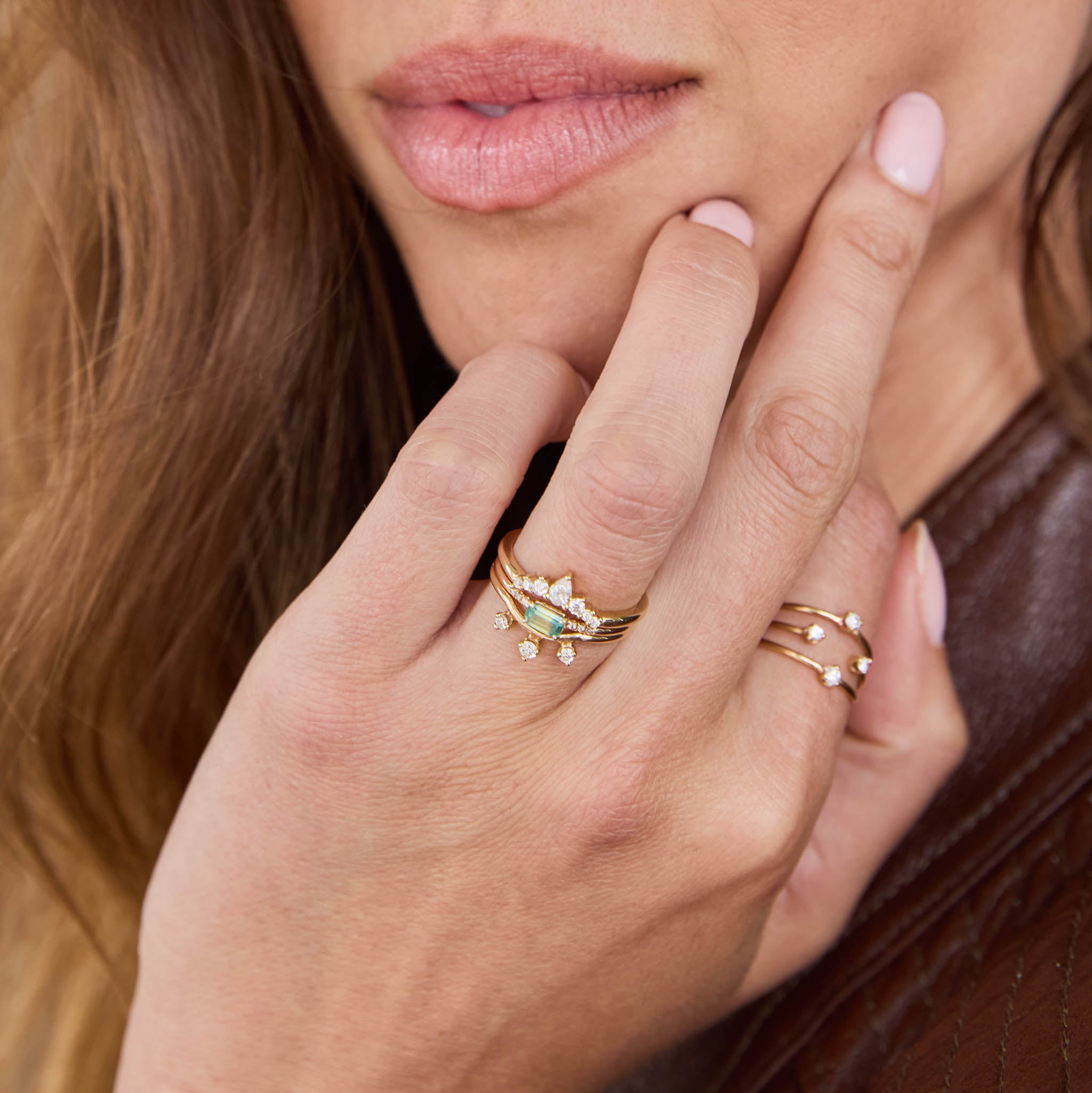 Zoe Chicco 14k Gold Close-up of a hand wearing multiple gold rings with gemstones, touching the face.