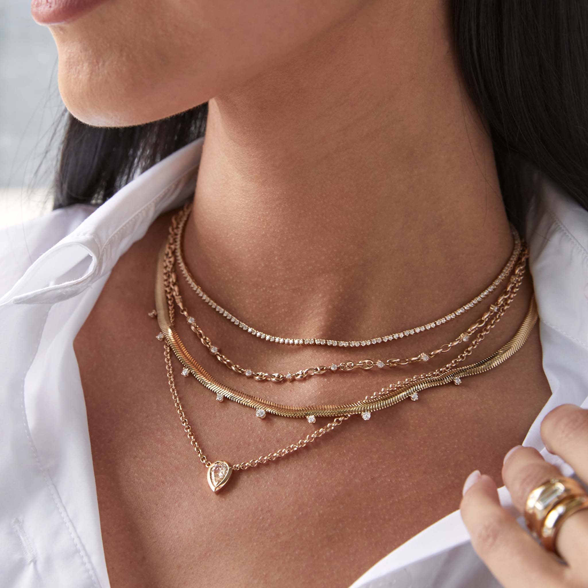 close up of a woman in a white shirt wearing a Zoë Chicco 14k Gold One of a Kind Mine Cut Pear Diamond Rolo Chain Necklace layered with a diamond tennis necklace, 14k Linked Prong Diamond & Small Puffed Mariner Chain Necklace, and a 14k 9 Graduated Prong Diamond Medium Snake Chain Necklace