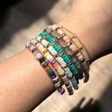 A close up of a woman's wrist wearing 7 different gemstone and 14k gold rondelle bead bracelets stacked together