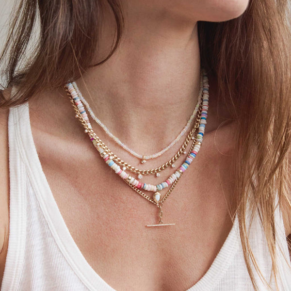 a woman in a white tank top wearing a Zoë Chicco 14k Gold & Fire Opal Rondelle Bead Necklace with Marquise Diamond layered with a Graduating Prong Diamond Curb Chain necklace and a 14k Mixed Small Curb & Medium Square Oval Chain Pavé Diamond Toggle Lariat Necklace