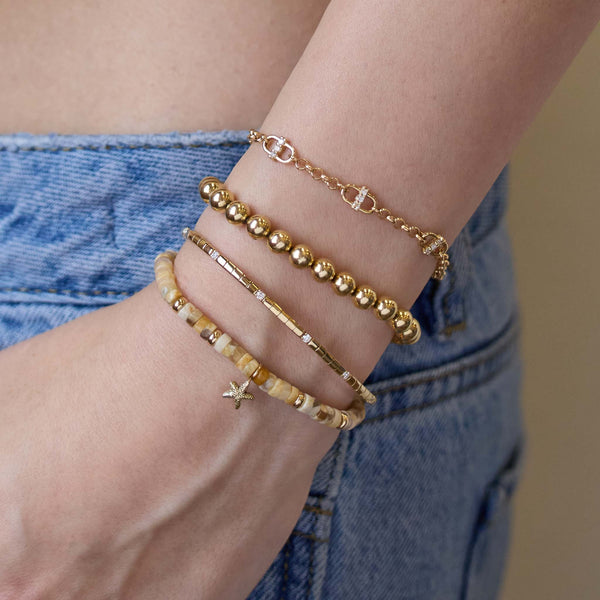 Gold bracelet stack on a model's wrist with a blurred denim background