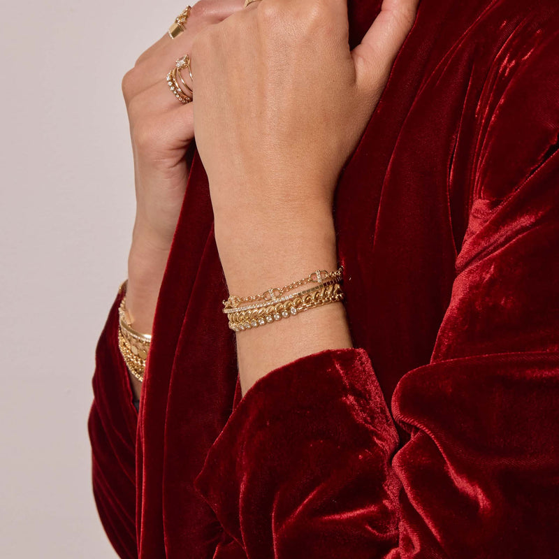 Close-up of a person wearing gold bracelets and rings on a red velvet garment.