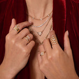 Close-up of hands wearing multiple Zoe Chicco 14k gold rings and necklaces with diamonds against a red velvet background